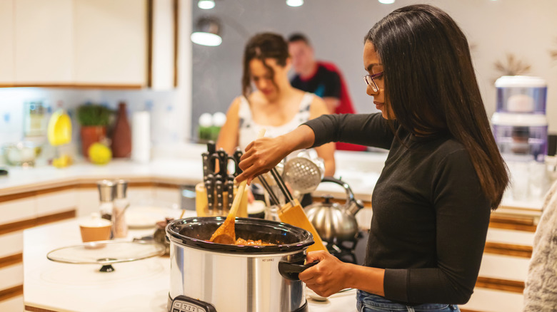 A woman serving herself from a slow cooker in a kitchen