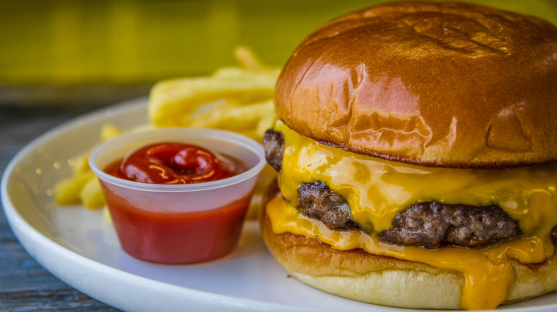 Cheeseburger with cheese melting from both above and below the patty, with ketchup and fries