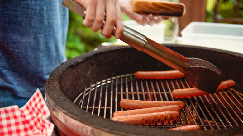 Person grilling several hot dogs outdoors over charcoal grill.