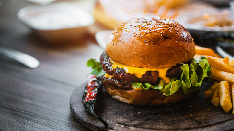 A burger served on a wooden board with fries
