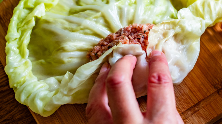 close up of hand rolling cabbage leaves around dumpling filling