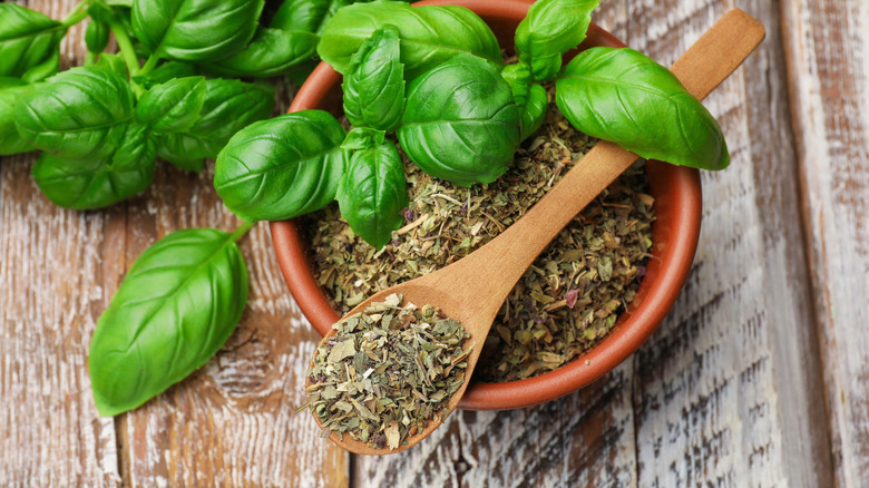 Spoonful of Italian seasoning and sprigs of fresh basil leaves