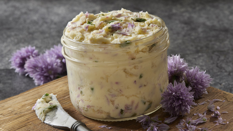 Compound butter in a glass jar on top of a cutting board, with purple flower blooms around the jar