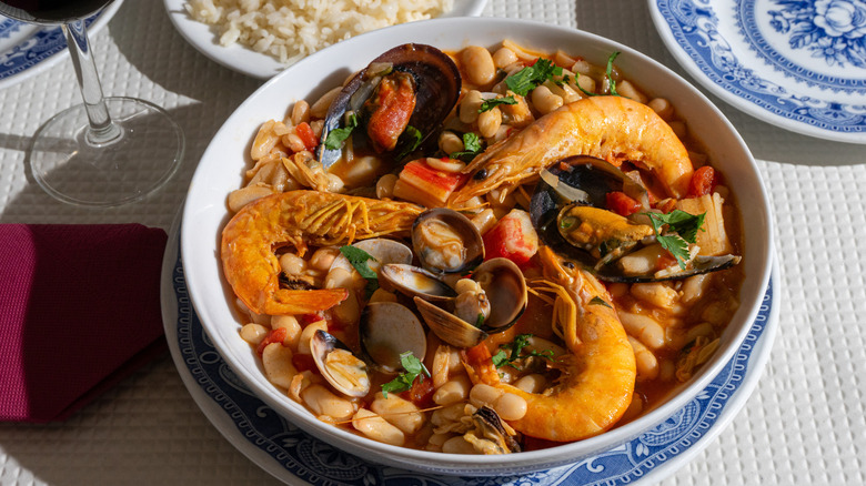 A vibrant seafood stew with white beans, prawns, and mussels in a wide bowl