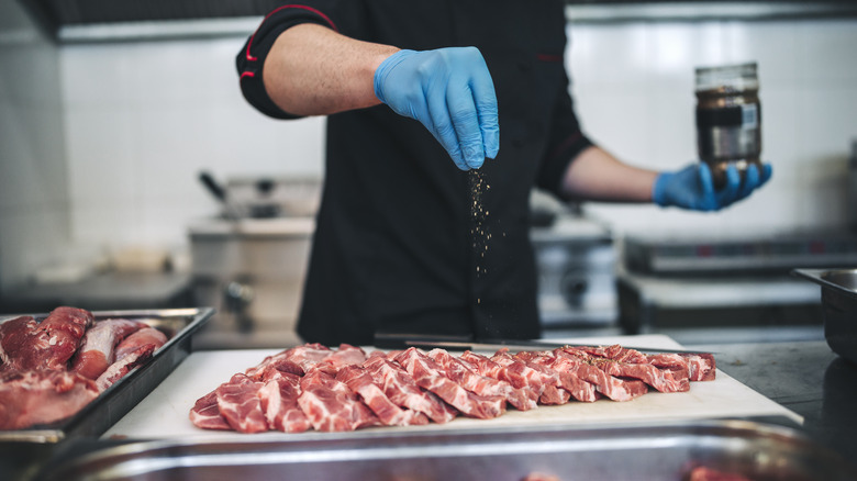 a gloved hand seasoning sliced meat on a cutting board