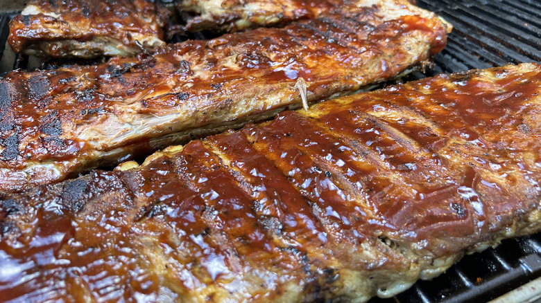Racks of pork ribs smoking on a grill with a sauce glaze on top