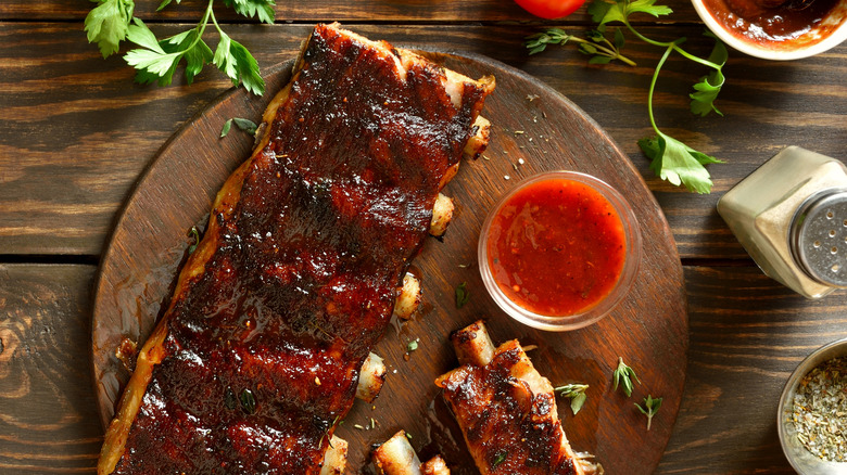 Ribs with a saucy glaze on a round wooden cutting board with more sauce to the side.