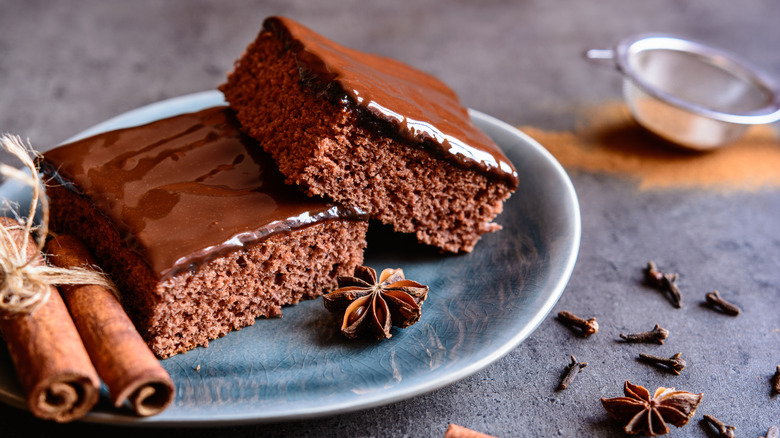 Two glazed brownie squares on a plate next to cinnamon sticks and star anise.