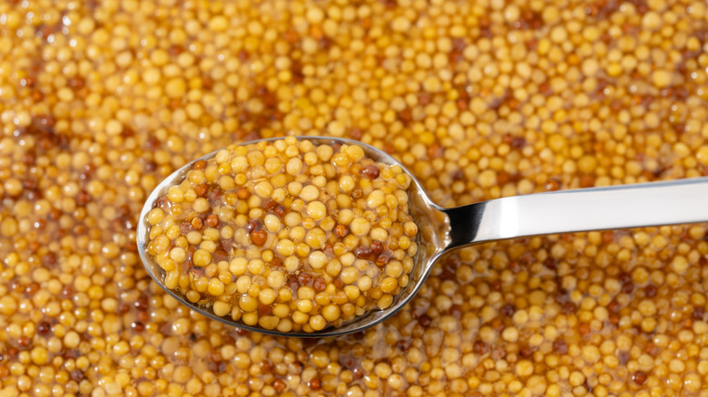 close up of Dijon mustard on metal spoon.