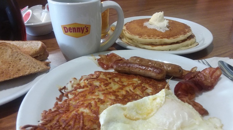 Denny's breakfast with hash browns, eggs, bacon, sausages, pancakes, toast, and coffee