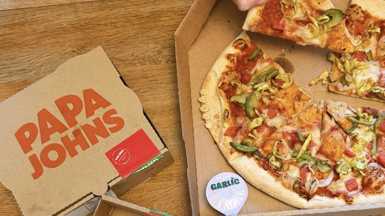A box of Papa John's pizza with the logo on the front is shown next to a pizza in a box.