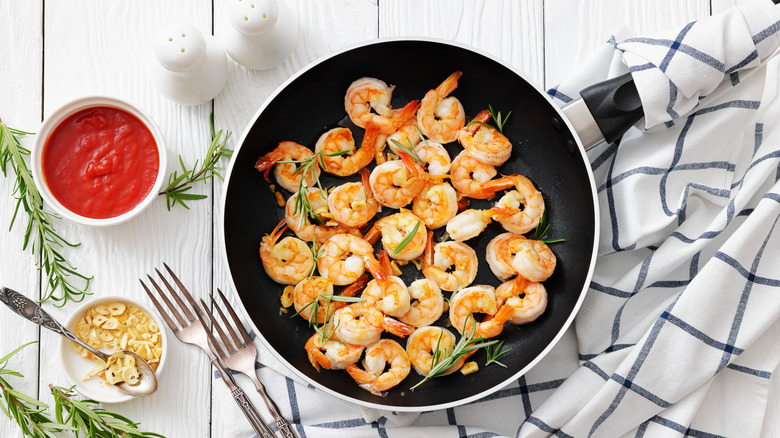 cooked shrimp in a pan with herbs and sauces on the side