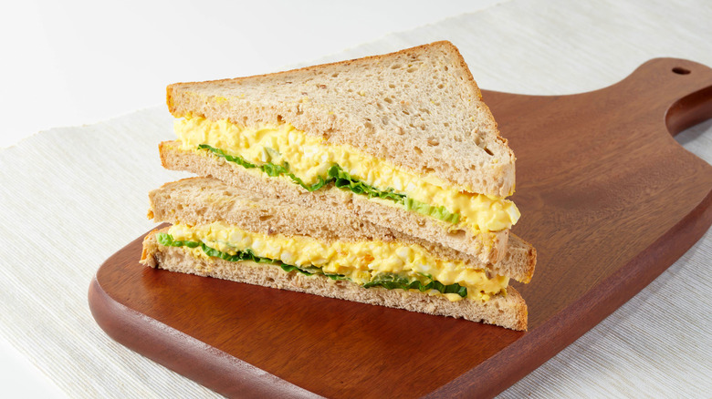 A sandwich made with egg salad on a wooden platter