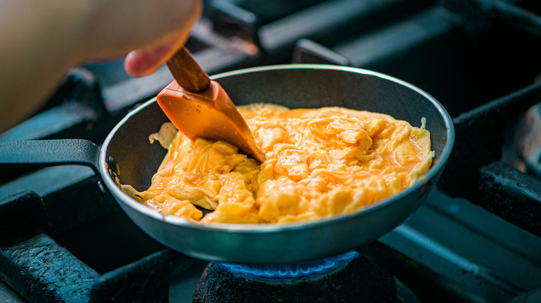 a spatula stirs scrambled eggs in a pan
