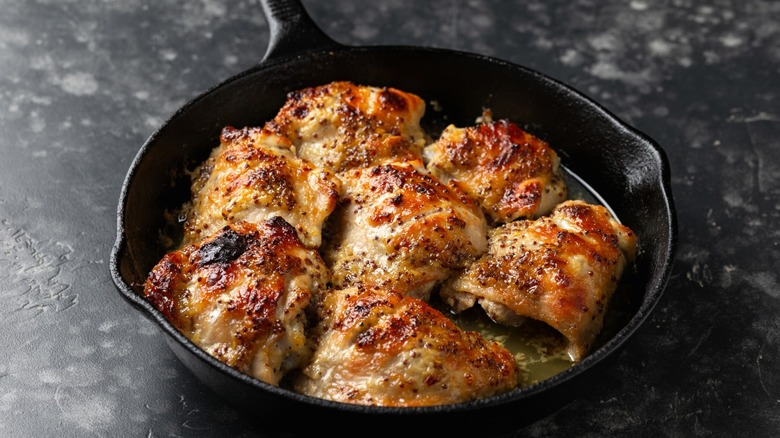 A cast iron skillet full of chicken sits on a gray marble counter