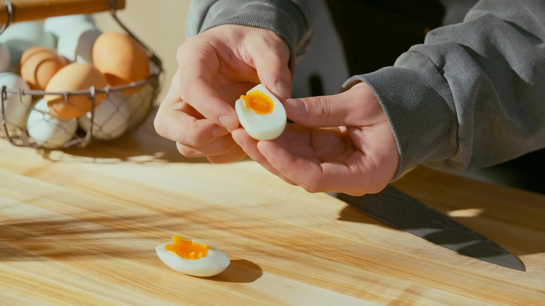 Hands holding one of two egg halves showing jammy yolk