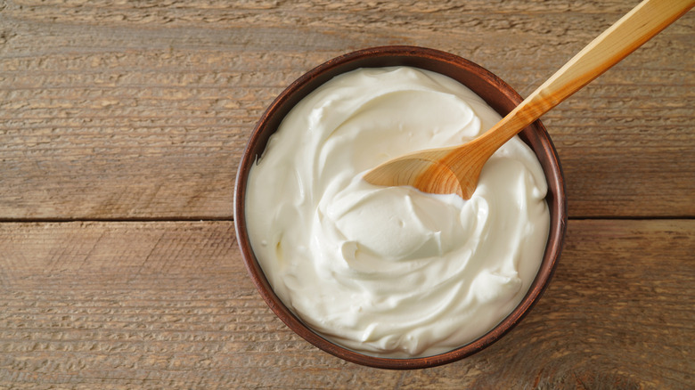 A bowl of sour cream on a wooden table with a wooden spoon inserted.