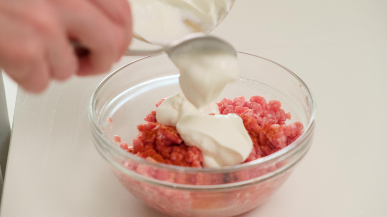 hand adding mayo to ground beef in a bowl