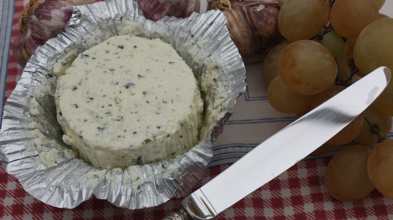Bourdin cheese in a foil wrapper with a knife, grapes, and garlic around it