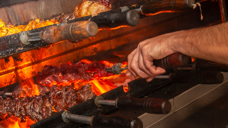 Hand turning skewered meat on grill at a Brazilian steakhouse