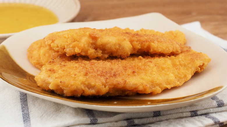 A serving board of crispy chicken tenders with a bowl of melted butter