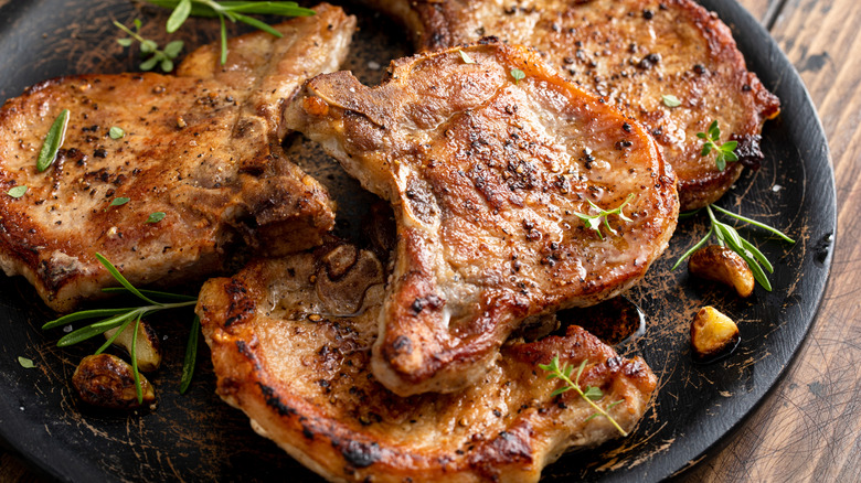Several cooked pork chops arranged on a dark plate on a wooden table