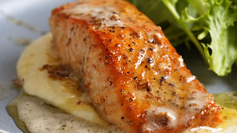 Salmon cooked with a butter sauce is served on a plate with greens.