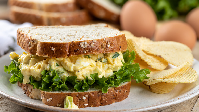 Egg salad and lettuce on multigrain bread next to some potato chips on a plate