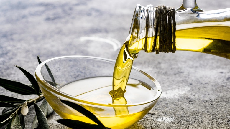 a glass jug of olive oil being poured into a glass bowl