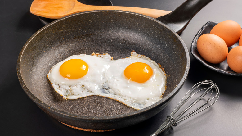 Fried eggs in a pan with a spatula and a whisk
