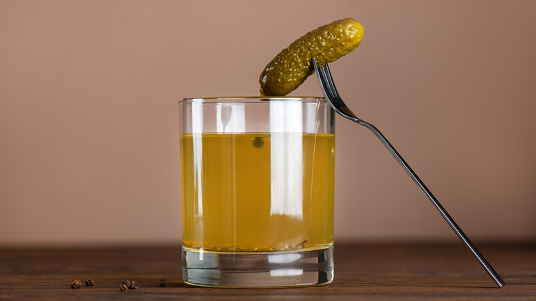 a glass filled with pickle juice and single pickle on fork