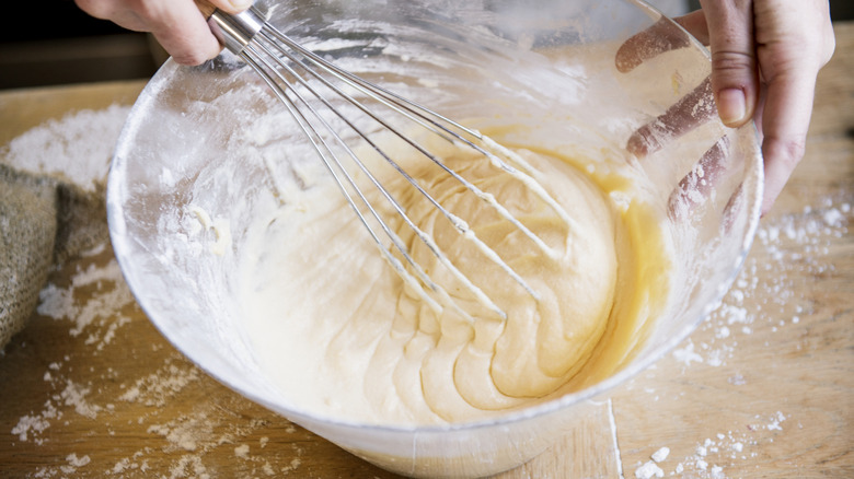 Person mixing cake batter with a whisk in a glass bowl