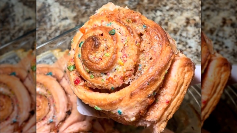 Fruity Pebbles Sweet Roll being held up beside a glass baking dish
