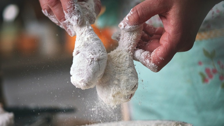 Someone coating chicken for frying