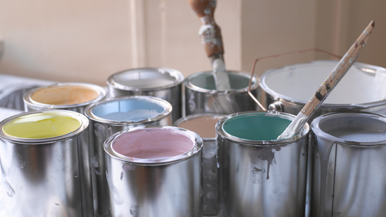 Several open tins of paint in different colors, two of which have either brushes or mixing sticks in them