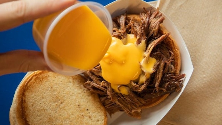 person pouring cheese sauce on Culver's beef pot roast sandwich