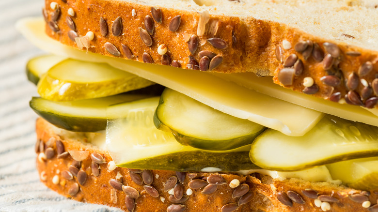 Close up of a sandwich made with a seed covered bread loaded with pickles