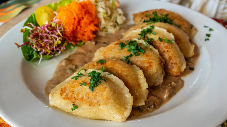 A row of golden fried pierogies on a sauced plate with garnishes on the side.