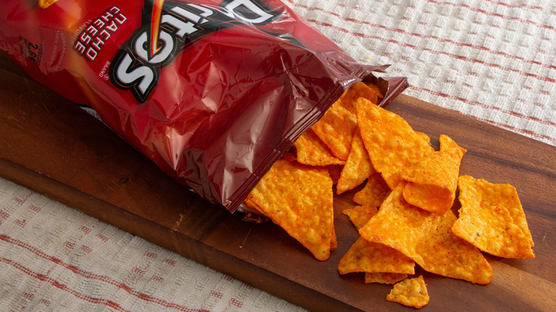 a bag of nacho cheese Doritos spilling out onto a wooden board