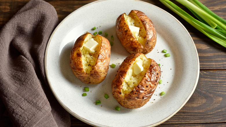 Homemade baked potatoes on a white plate, garnished with butter pats and green onions