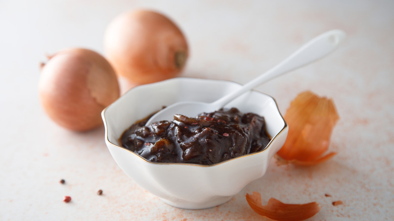A bowl of onion confit and spoon with onions in the background