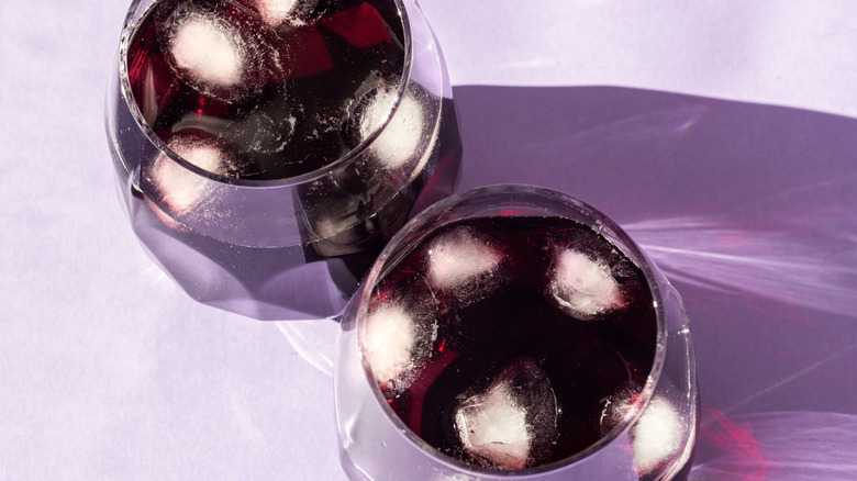 Two glasses of lambrusco wine with ice atop a light purple background.