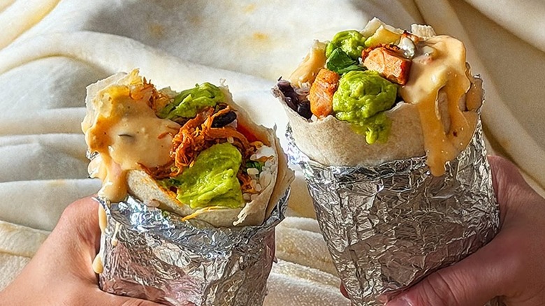 Two people holding burritos from Qdoba