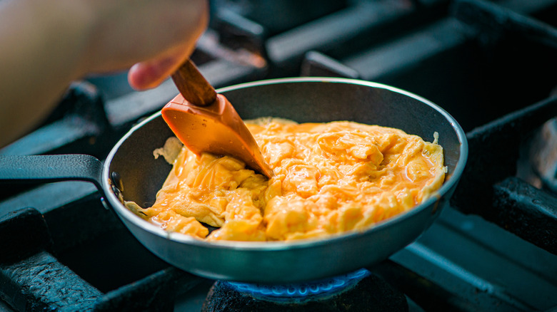 Person cooking scrambled eggs in a frying pan on a gas stove burner