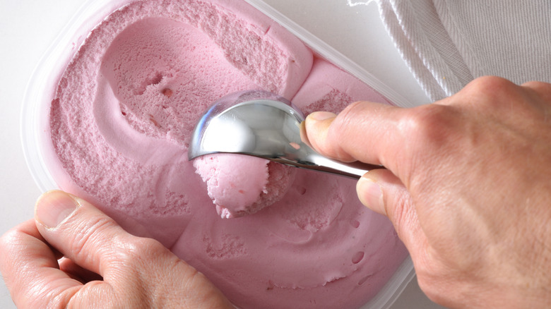 close up of person making a scoop of strawberry ice cream on white table