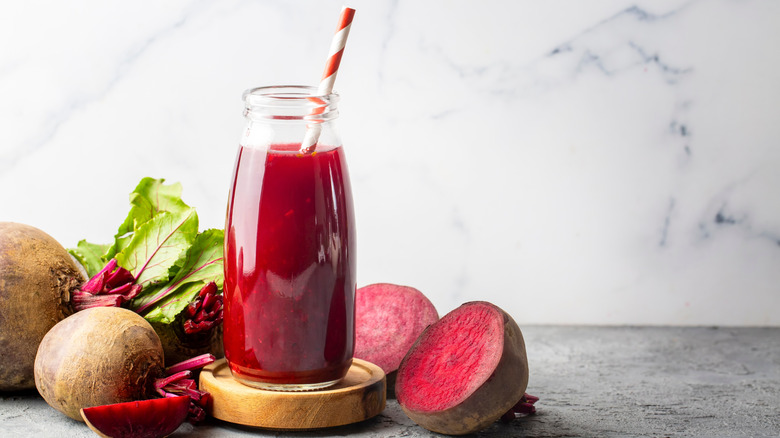 Glass bottle of beetroot juice next to raw beets, against marbled backdrop