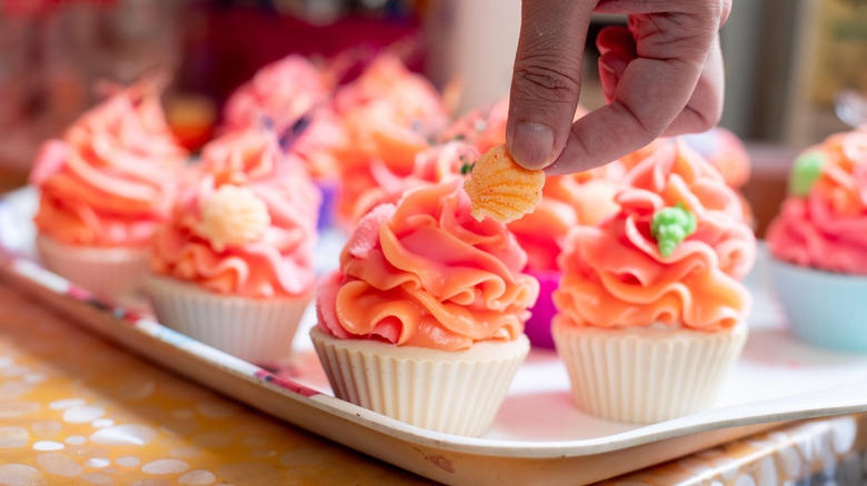 Topping cupcakes with pink and orange icing with a sugar figure