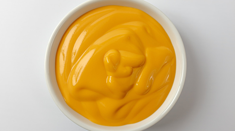 A top-down view of a small white bowl filled with creamy yellow cheese sauce.