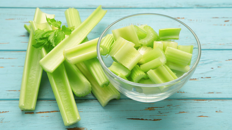 Celery stalks beside a bowl of chopped celery