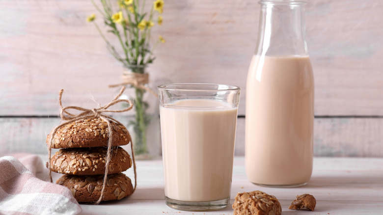 Chocolate milk in glass cup and jar with stacked oat cookies nearby